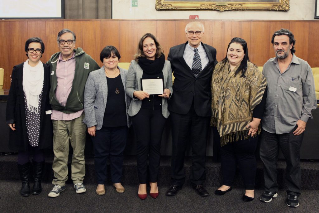 Daniella Meggiolaro, diretora do IDDD responsável pelo projeto, recebe a placa de menção honrosa entregue pelo vereador Eduardo Suplicy, que presidiu a sessão solene da premiação